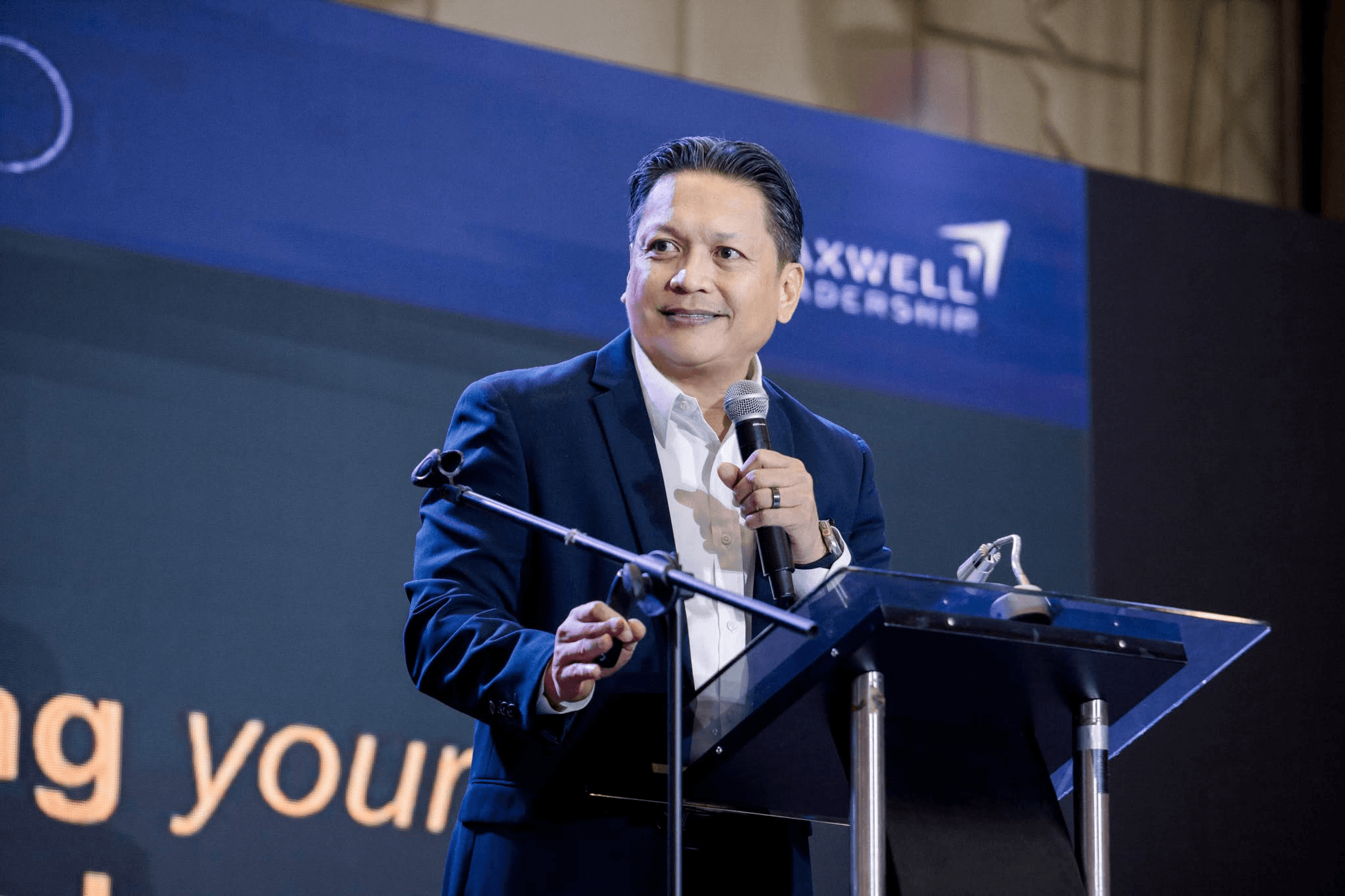 Coach Jon Engalla speaking on stage at a Maxwell Leadership event